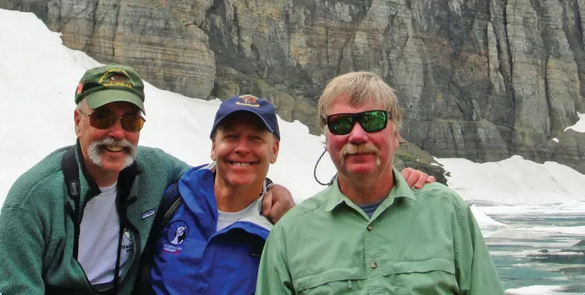Chris Servheen with two colleagues in front of a glacier and cliff face