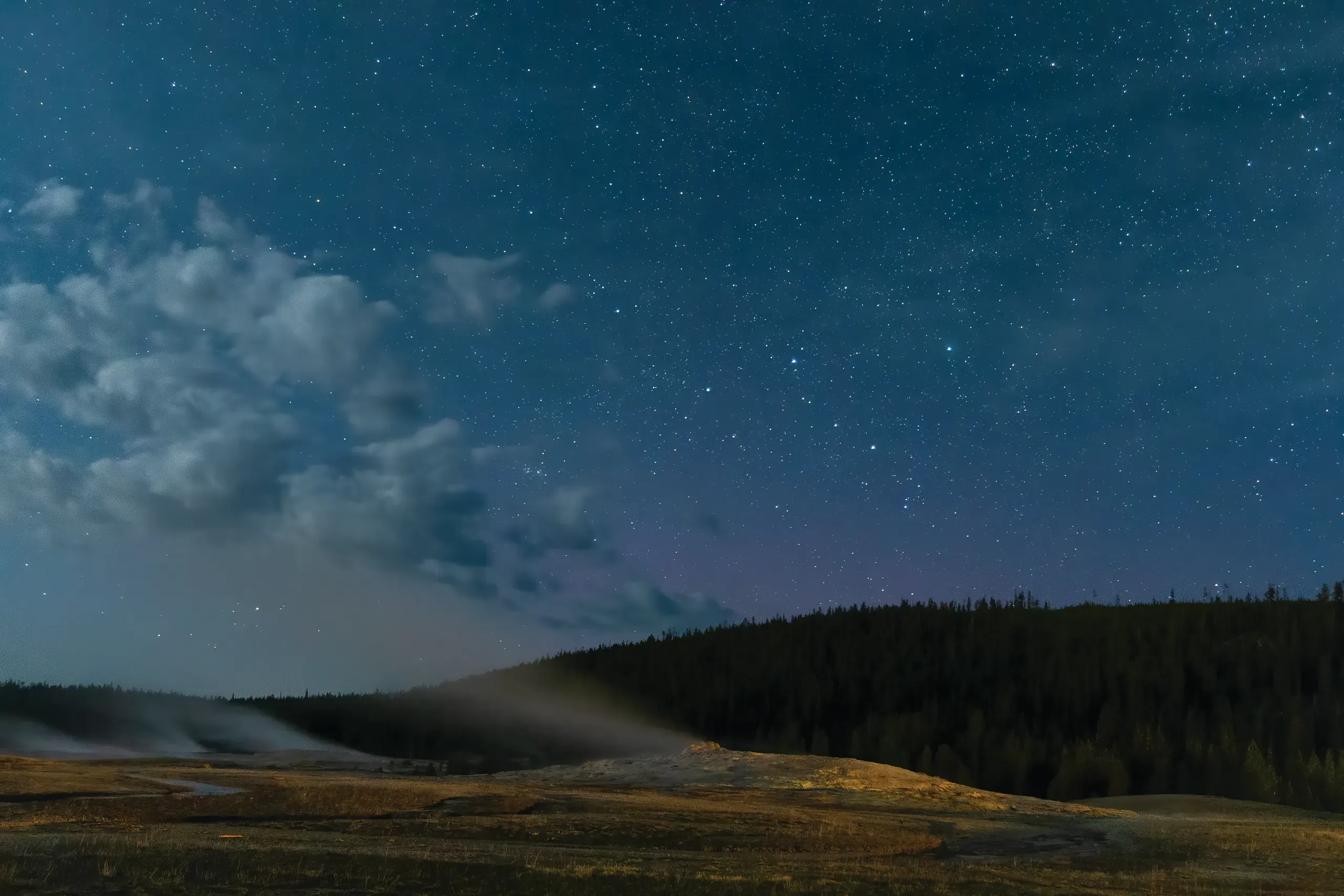 Turning Down The Lights 3 Old Faithful steaming under a star-filled night sky in Yellowstone